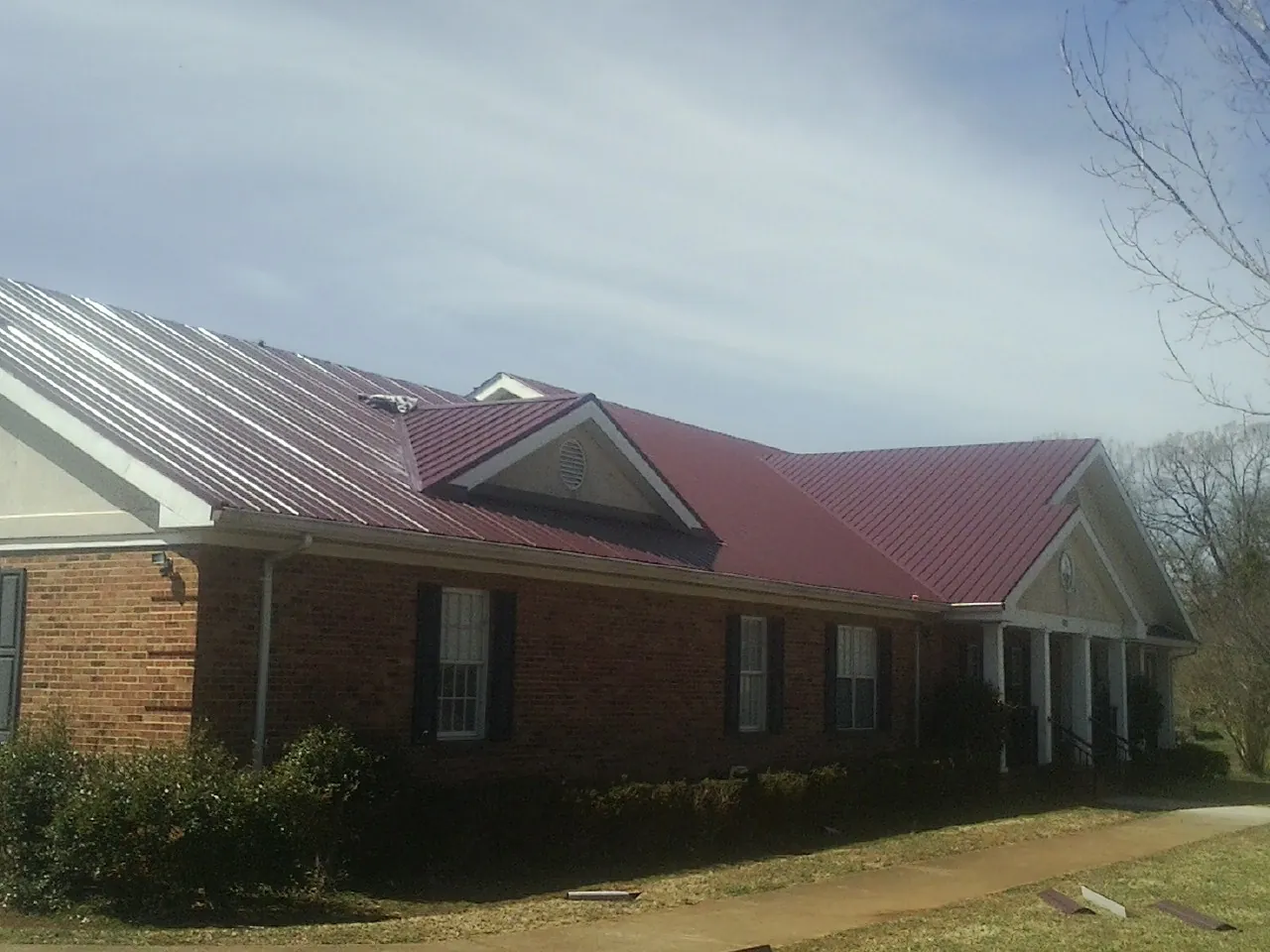 Red metal roof with gabled entries on a long brick building, from a Hail Damage Roof Repair job in Phoenixville