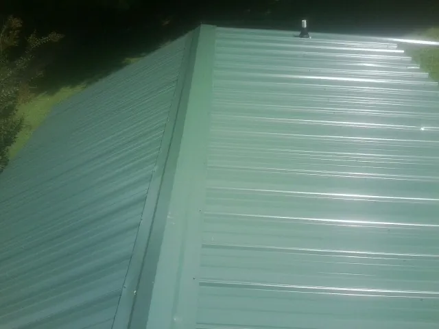New green metal panels meeting at the ridge of a roof — Flat Roof Repair work by our crew in Phoenixville
