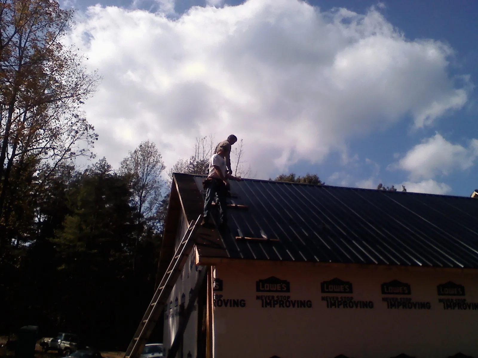 Roofer fastening dark metal panels high against a cloudy sky, from a Roof Inspection job in Phoenixville