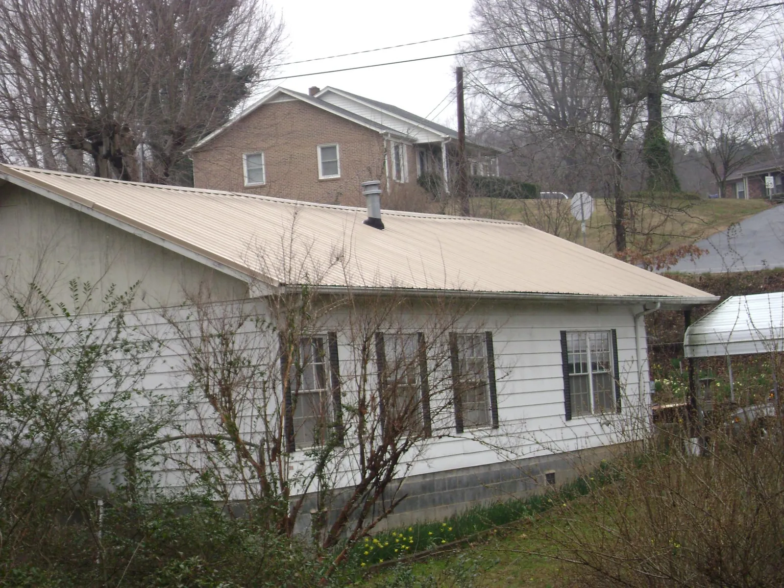 Tan metal roof on a white sided house set into a hillside — Commercial Roofing by Roofing Brothers in Phoenixville
